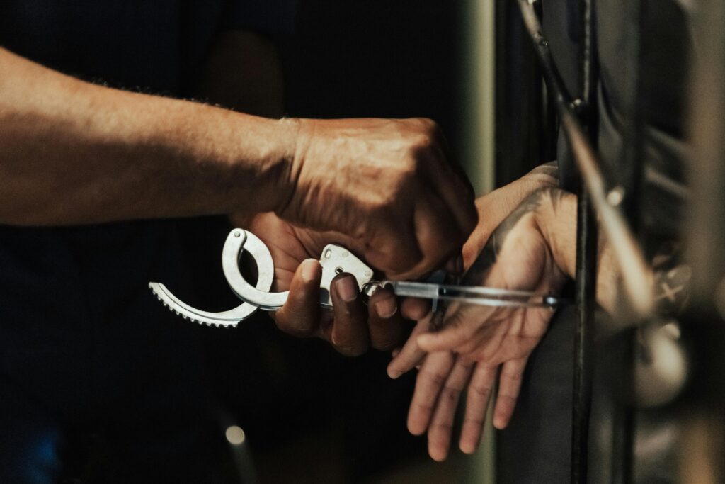 Close-up view of a person being handcuffed in a jail setting, focusing on hands and handcuffs.