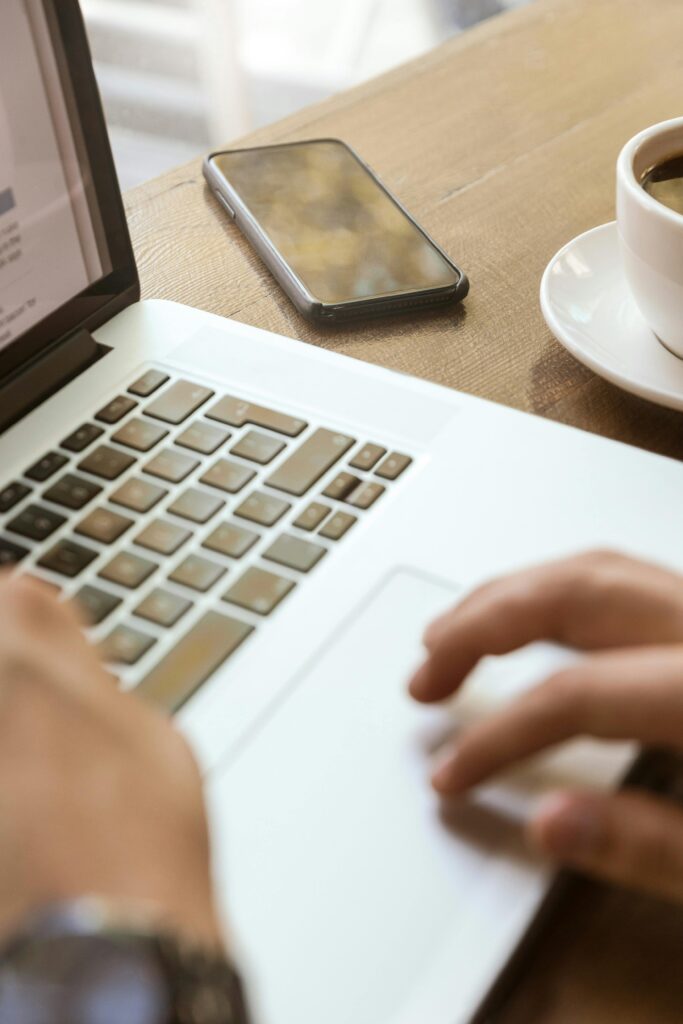 Close-up of hands typing on a laptop with a smartphone and coffee, depicting a modern workspace.