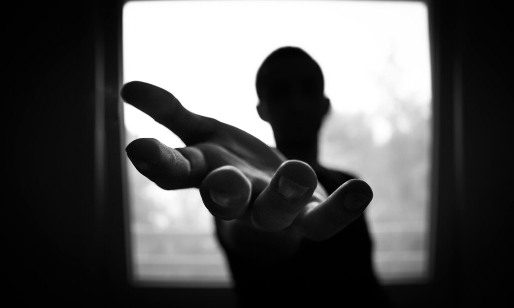 Silhouette of a hand reaching out in a black and white contrast.