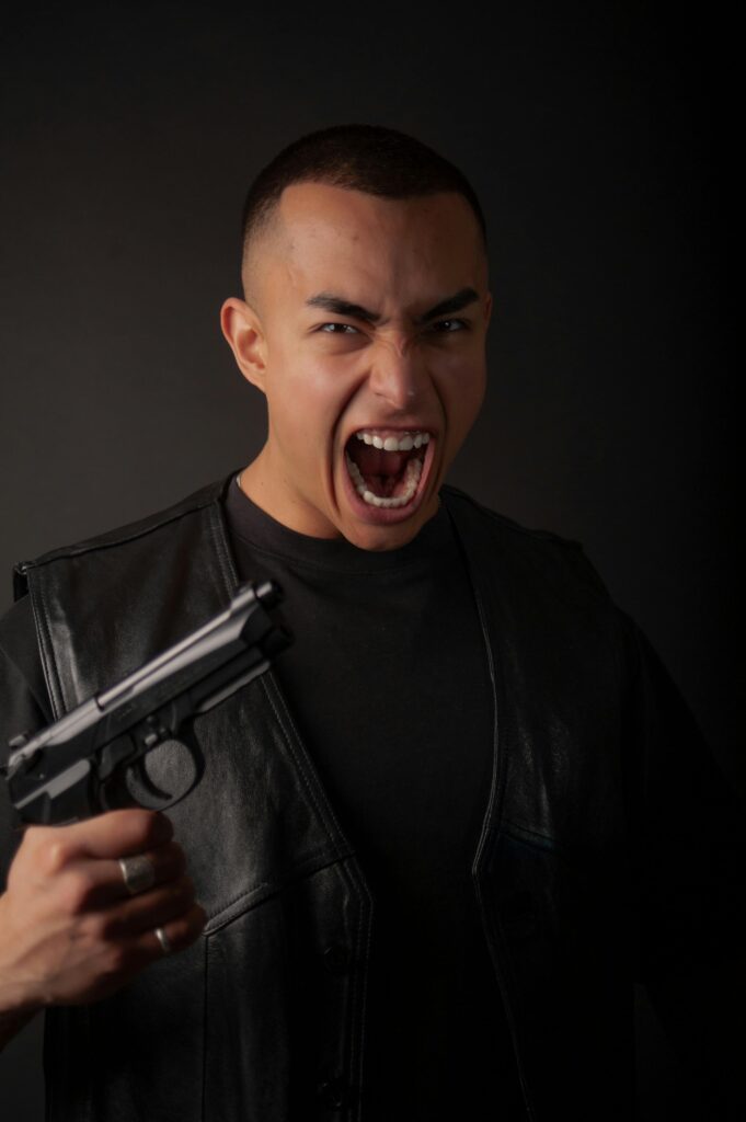 Intense portrait of a man yelling with a gun, expressing strong emotion in a dark setting.