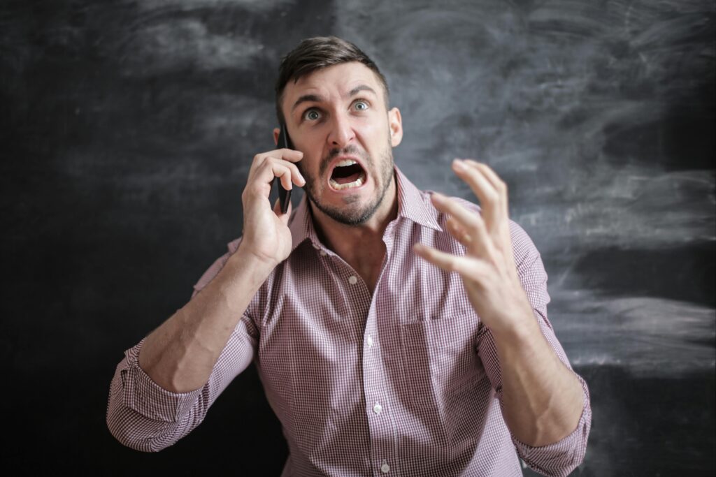 A distressed man in a pink shirt expressing frustration while using a smartphone indoors.