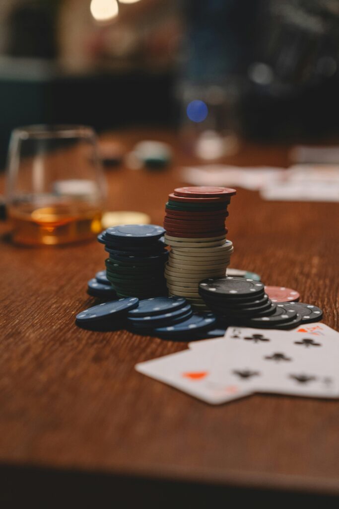 Poker chips and playing cards on a wooden table with a whiskey glass, emphasizing gambling and entertainment.