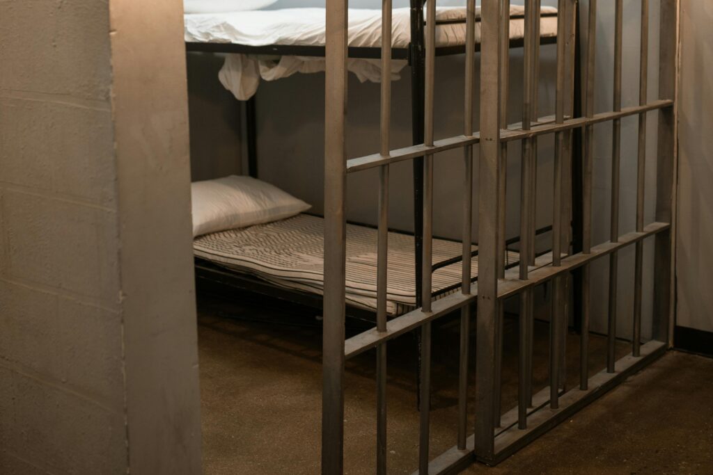 pexels-photo-6064890-6064890 A prison cell featuring a metal bunk bed and striped sheets.